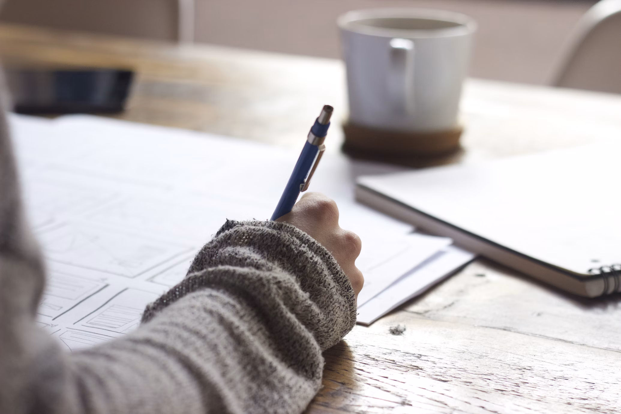 Une main annote une feuille au stylo à côté d’une tasse et d’un carnet : ce sont les petits ajustements quotidiens qui construisent la progression