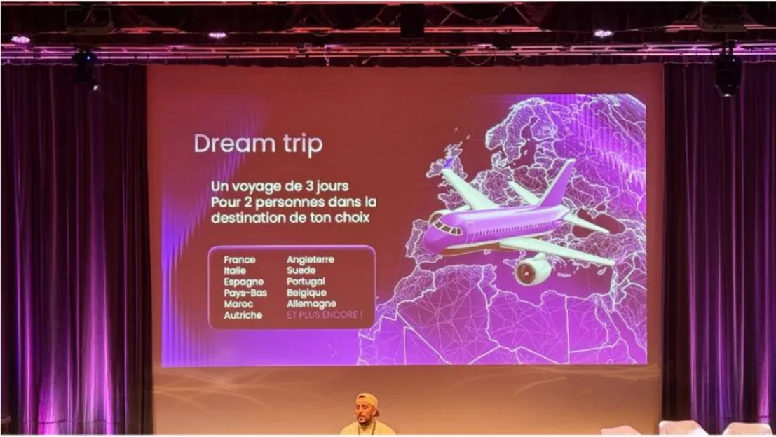 Sur la scène d’une convention, une diapositive « Dream trip » annonce un voyage de trois jours pour deux personnes vers la destination de son choix, parmi une douzaine de pays