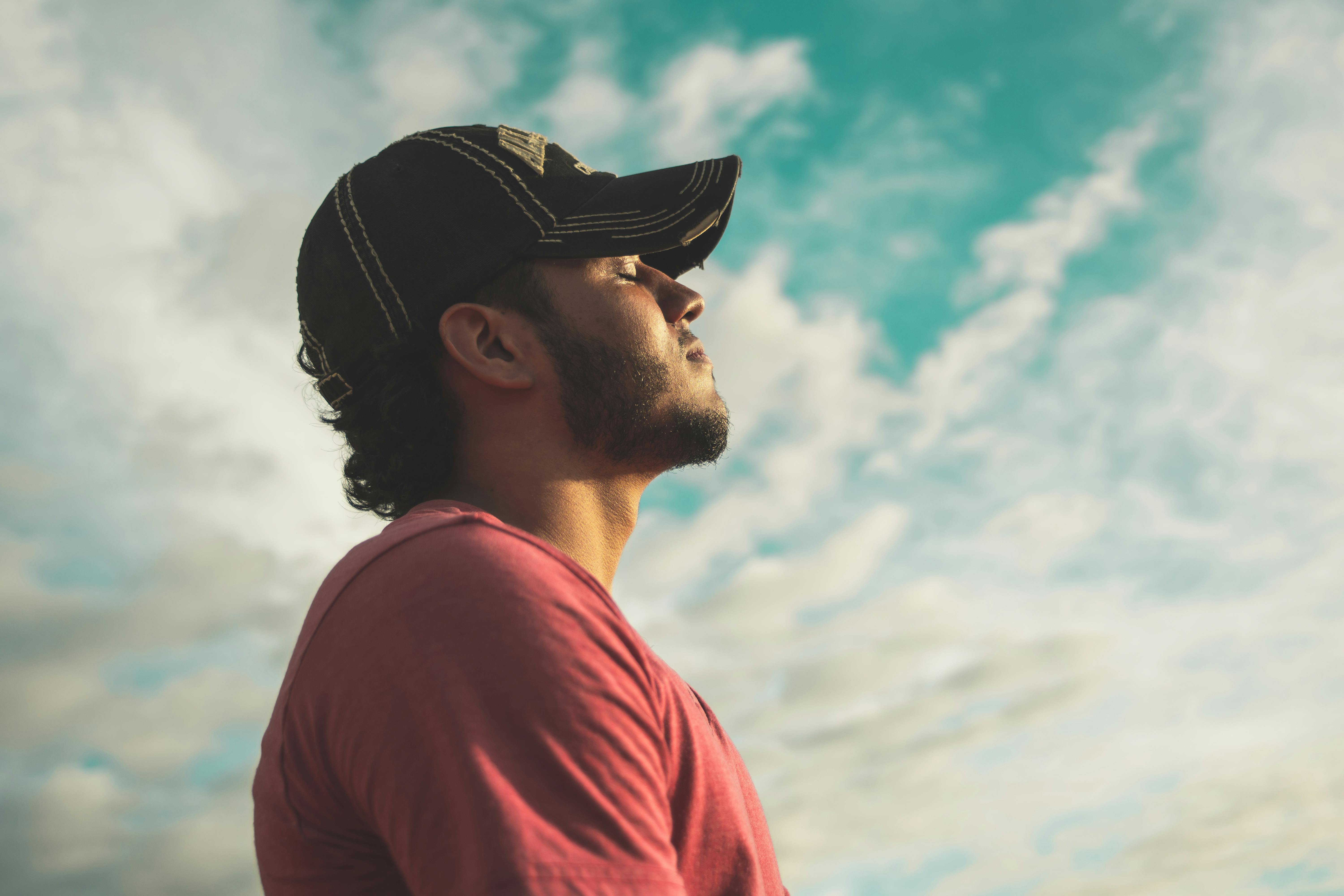 Un homme en casquette, les yeux fermés et le visage tourné vers le ciel, respirant calmement : reprendre la main sur ses émotions plutôt que les subir
